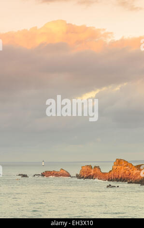 Cliffs under big cloudy sky with lighthouse in distance, rocks illuminated by last sun rays before sunset, sunlight, Saint Malo, Stock Photo