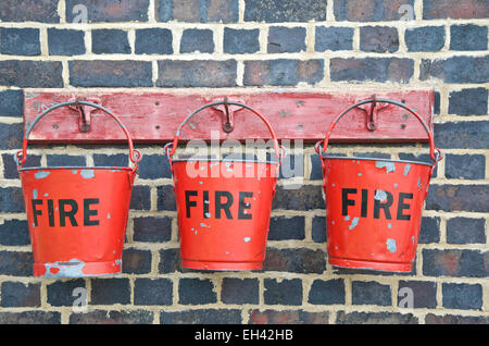 Three red fire buckets hanging against a brick wall Stock Photo