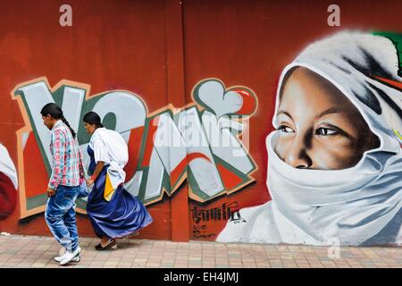 Ecuador, Imbabura, Atuntaqui, modern Ecuadorian pair past a wall graffiti depicting a veiled woman Stock Photo