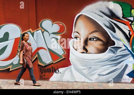 Ecuador, Imbabura, Atuntaqui, Ecuadorian busy modern woman in front of a wall graffiti depicting a veiled woman Stock Photo