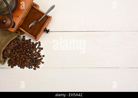 High angle shot of a bag of coffee beans and an antique  grinder on a rustic white wood table. The items are in the upper left c Stock Photo