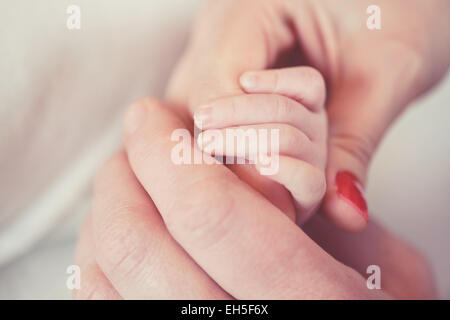 Parents' hands hold the fingers of newborn baby The hand of a mother ...