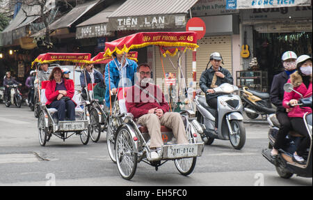 Mature,elderly, tourists in rickshaws being driven around on a sightseeing tour of the Old Quarter, Hanoi, Vietnam. Stock Photo