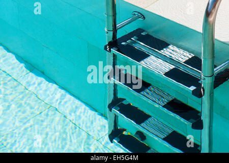 Close-up of ladder in swimming pool water on sunny day, soft focus Stock Photo
