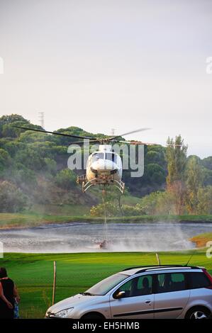Bell 412 registration EC-IPM collecting water for fire fighting from a golf club lake, Cabopino Golf, Costa del Sol, Spain. Stock Photo