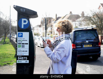 Female driver pays for parking meter using a paybyphone mobile phone app in Brighton UK Stock Photo