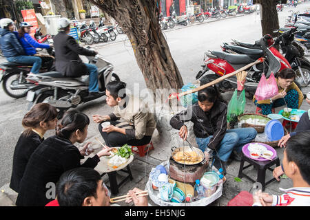 Sitting on plastic stools for a street food meal on the scooter filled pavement and passing scooters in Han Noi, Hanoi,Vietnam, Stock Photo