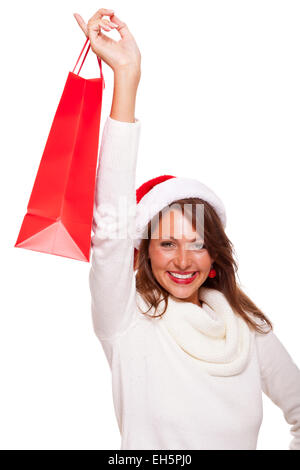 Happy vivacious Christmas shopper wearing a red Santa hat holding up a colorful red shopping bag with a beautiful beaming smile, Stock Photo