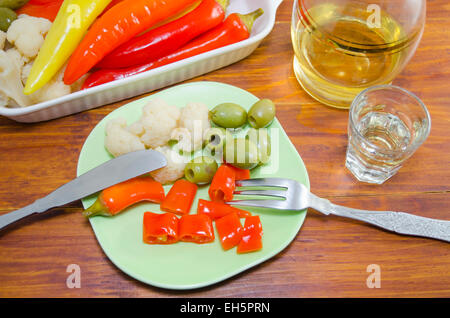 Pickled peppers, cauliflower and olives on a plate with a knife and a fork and a shot of brandy Stock Photo
