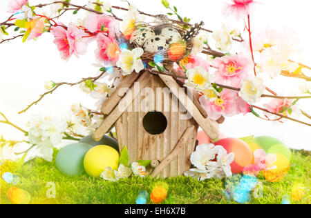 Easter decoration with birdhouse and eggs on green grass. Spring apple and cherry blossoms. Retro style toned picture with light