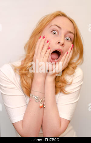 Close up portrait of a young caucusian woman with curly blond hair scared, afraid and anxious. Screaming, with eyes wide open. Stock Photo
