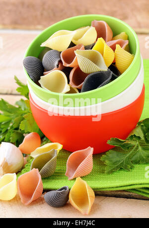 uncooked tricolor pasta in bowl on a wooden table Stock Photo