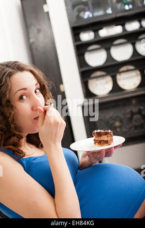 Pregnant woman in the kitchen eating cake. Stock Photo