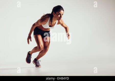 Young woman starting to run and accelerating over grey background. Powerful young female athlete running in competition. Stock Photo