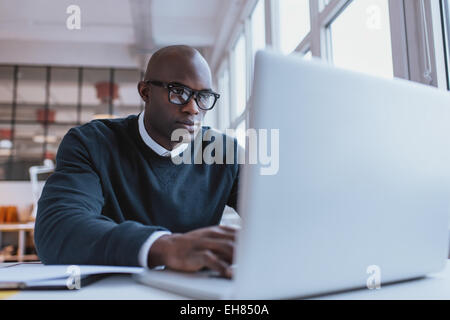 Young businessman working on his laptop in office. Young african executive sitting at his desk surfing internet on laptop comput Stock Photo