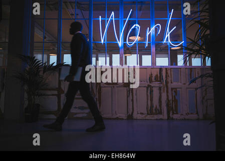 Corridor of a modern office with a neon work sign and executive walking by. Stock Photo