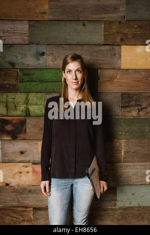 Portrait of beautiful young businesswoman standing against a wooden wall looking at camera. Caucasian woman in casuals in office Stock Photo