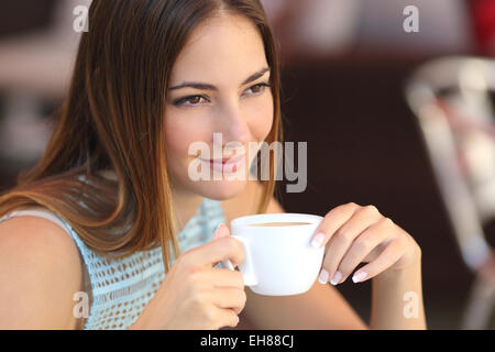 Candid woman thinking in a coffee shop holding a cup with an unfocused background Stock Photo