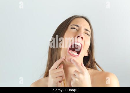 Girl crying while pressing a pimple on her chin with a grey background Stock Photo