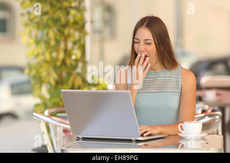 Tired woman yawning and working with a laptop in a restaurant during breakfast Stock Photo