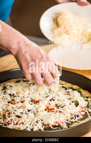 Woman sprinkling grated swiss cheese on an unbaked vegetarian, multi-grain thick-crust pizza Stock Photo