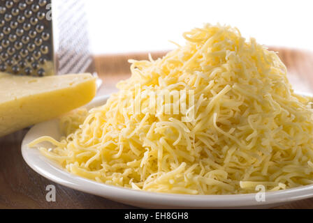 Grated cheese on a plate. Grater and piece of cheese in the background. Stock Photo