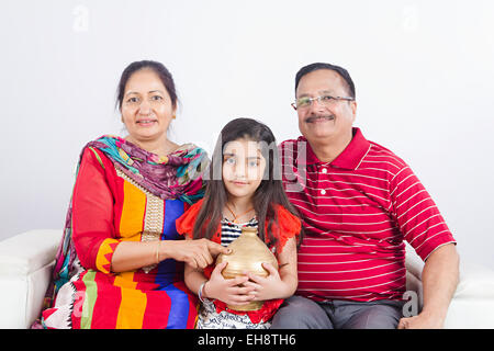 3 indian grand parents and kid  Grand daughter sitting sofa Piggy Bank Saving money Stock Photo