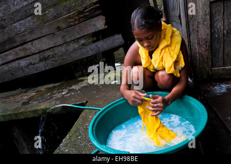 A Colombian girl washes clothes in a bucket, outside a wooden house in the stilt house area in Tumaco, Colombia. Stock Photo