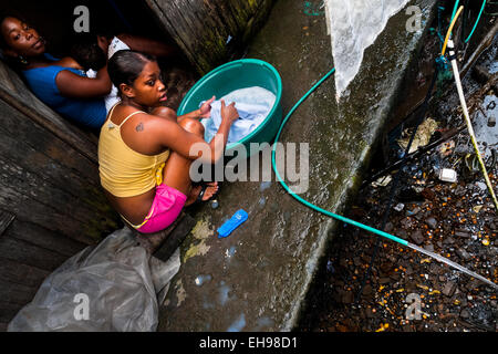 A Colombian girl washes clothes in a bucket, outside a wooden house in the stilt house area in Tumaco, Colombia. Stock Photo