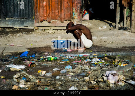 A Haitian woman bathes in a bucket outside the sheet-metal houses in a shanty town close to La Saline market, Port-au-Prince, Haiti. Stock Photo