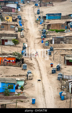 A Peruvian woman with her child climb up a steep path along the plastic water containers on the dusty hillside in Lima, Peru. Stock Photo