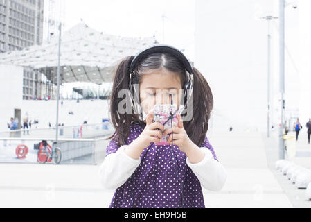 Girl looking at smartphone and listening to headphones outdoors Stock Photo