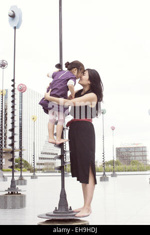 Mother and daughter nuzzling while standing on whimsical sculpture Stock Photo