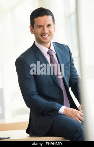 Businessman sitting on edge of table, smiling, portrait Stock Photo