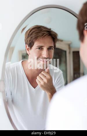 Man looking at self in mirror touching facial stubble Stock Photo