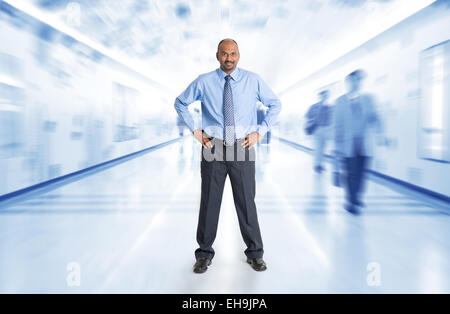 Full body Indian businessman standing at corridor, inside business building with motion blurred people as background. Stock Photo