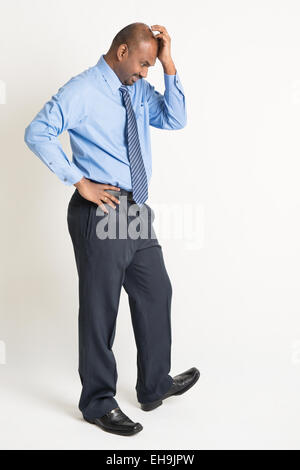 Full length Indian businessman with worried expression standing on plain background with shadow. Stock Photo