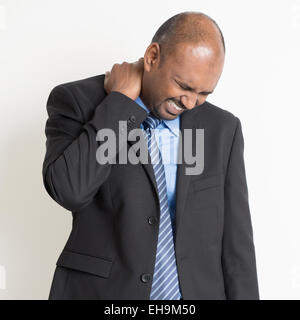 Indian businessman shoulder pain, holding his neck with painful face expression, standing on plain background. Stock Photo