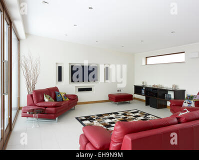 Modern living room with red leather sofas and built in plasma TV and speakers in Shirley Drive home, UK Stock Photo