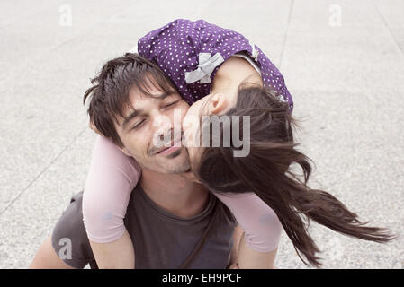 Little girl riding on father's shoulders, kissing his cheek Stock Photo