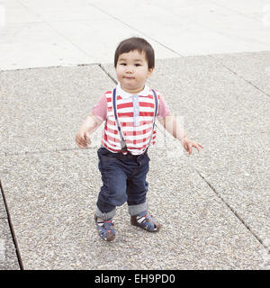 Baby boy walking on sidewalk with snack in hand Stock Photo