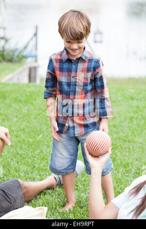 Boy playing ball at lakeside park with family Stock Photo