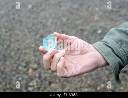 A man's hand holding a large piece of aqua-colored sea glass. Stock Photo