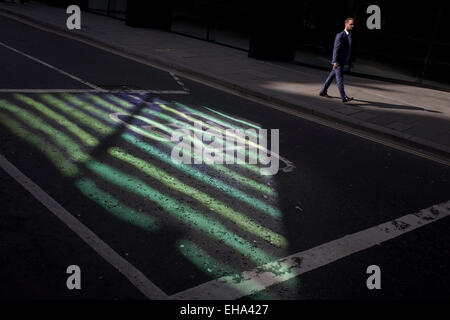 Pedestrian walks past reflected green light from nearby office building plate glass. Stock Photo