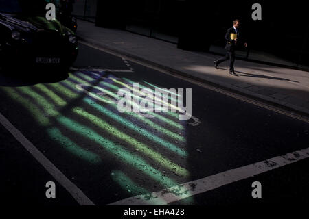 Pedestrian walks past reflected green light from nearby office building plate glass. Stock Photo