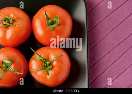 Fresh tomatoes placed in a black ceramic plate Stock Photo