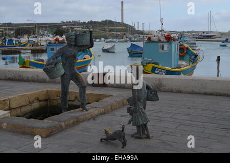 This isalongside the quay at Marsaxlokk (Pro.Marsa-shlock).It shows a man watched by a boy,his sister,and dog doing the washing. Stock Photo