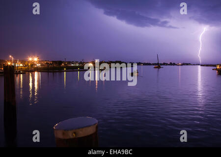 Lightning striking down over the harbor with a purple sky and a boat in the water. Stock Photo