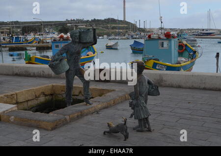 This isalongside the quay at Marsaxlokk (Pro.Marsa-shlock).It shows a man watched by a boy,his sister,and dog doing the washing. Stock Photo