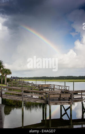 A rainbow arches over thick clouds after a storm. It reflects in the quiet waters of the intercoastal waterway Stock Photo